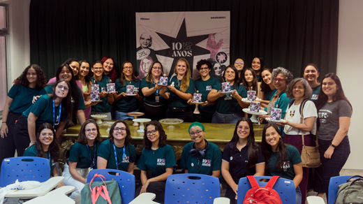 Na ocasião, comissão organizadora e convidadas do evento comemoraram os 10 anos do projeto com bolos de aniversário e parabéns. (Foto: Beatriz Machado/ PET-TI Quixadá) Imagem: Comissão organizadora do InfoGirl posa com as convidadas do evento. Elas seguram 10 minibolos de aniversário.