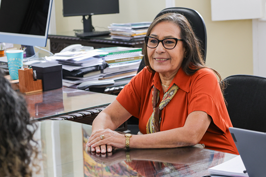 Imagem: Plano fechado da secretária Fátima Bandeira. Ela é uma mulher branca, de cabelos lisos e óculos, trajando blusa laranja.