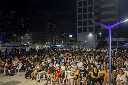 Pessoas reunidas sentadas nas cadeiras, durante a inauguração da praça