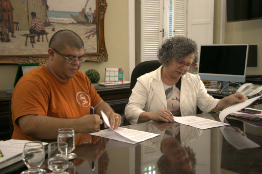 O coordenador-geral do SINTUFCE, Wagner Pires, e a vice-reitora da UFC, Profª Diana Azevedo, assinam o termo de acordo (Foto: Nilson Filho/UFC Informa) Imagem: Foto com o coordenador-geral do Sintufce, Wagner Pires, de blusa laranja, assinando o termo junto com a vice-reitora da UFC, Profª Diana Azevedo