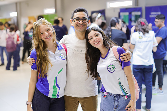 Professor Renato Vieira, egresso do curso de Geografia, se emociona em retornar à UFC acompanhando seus alunos (Foto: Ribamar Neto/UFC) Fotografia do Professor Renato com duas de suas estudantes em visita à Feira das Profissões da UFC (Foto: Ribamar Neto/UFC)