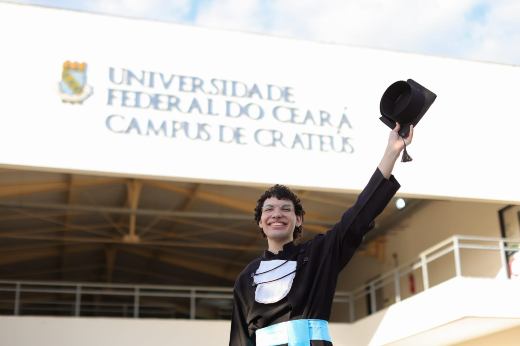 Imagem: estudante vestindo beca posa para foto em frente ao Campus de Crateús