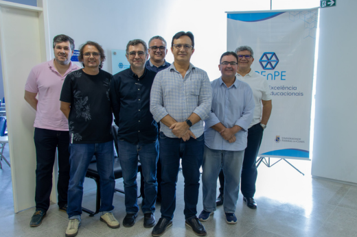 Professores posando para a foto no corredor do CEnPE. Atrás do grupo tem um banner com o logotipo do Centro