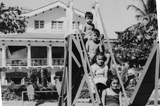Imagem: Foto em preto e branco com quatro crianças sentadas em um escorregador de parquinho infantil