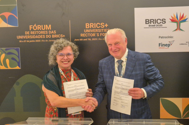 Imagem: uma mulher branca de cabelos grisalho e cacheados aperta a mão de um homem branco de termo e cabelos brancos. Os dois seguram, cada um, um papel com a outra mão