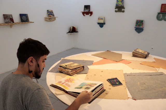 A exposição "Livro do artista: tramas" propõe um mergulho nas possibilidades sensíveis e inventivas do papel (Foto: Regis Torquato Tavares) Imagem: Homem folheia livro em ambiente de museu