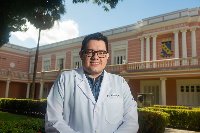 Imagem: Homem usando jaleco posa para foto em frente à Reitoria da UFC 