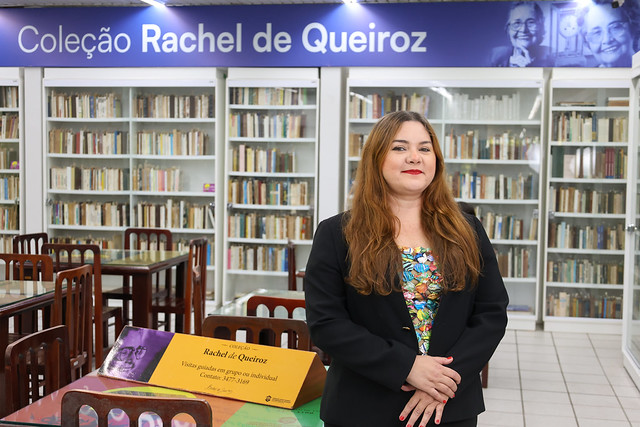 Imagem: Pesquisadora posa para foto em frente a uma estante de livros 