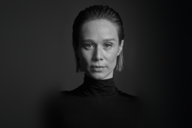 Imagem: Retrato frontal em preto e branco de Mariana Ximenes, mulher branca, loura. Ela veste blusa preta e tem os cabelos penteador para trás