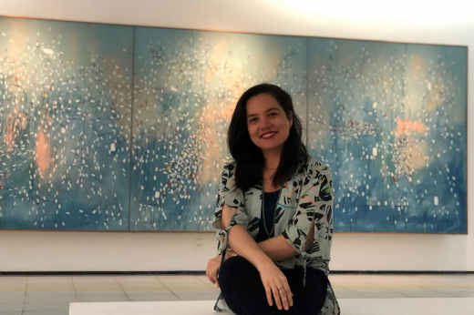 A atual diretora Graciele Siqueira assumiu o MAUC em 2018; ao fundo, o tríptico "Cidade em Festa", de Antônio Bandeira, após restauração (Foto: Natália Jessica) Imagem: a diretora do MAUC, Graciele Siqueira, sentado em banco no museu, com tela de Antônio Bandeira ao fundo