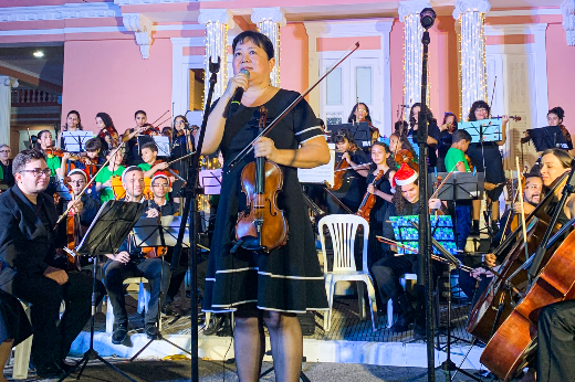 A professora Liu Man Ying, à frente da Camerata de Cordas e da Orquestra de Cordas da UFC: concerto que reuniu os dois grupos abriu a programação musical da noite (Foto: divulgação) professora do ICA aparece segurando um violino, de vestido preto e cabelo preso, à frente da Orquestra e da Camerata de Cordas da UFC, com músicos sentados segurando seus instrumentos, vestidos de preto