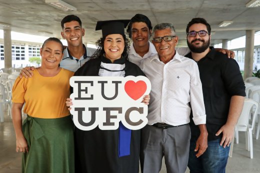 Natacha Falcão celebrou junto à família e ao namorado, também graduado pela UFC, no mesmo campus. Agora os dois são profissionais de Engenharia Civil (Foto: Ribamar Neto/UFC) Imagem: Formanda Natacha Falcão posa junto à família e ao namorado, segurando uma placa onde se lê Eu Amo UFC (com a figura de um coração vermelho no lugar da palavra "amo")