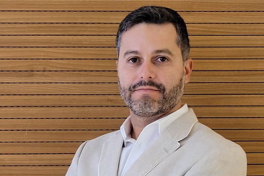 Professor Yuri Lima lidera grupo de pesquisa na área de Sistemas Dinâmicos e Teoria Ergódica, no Departamento de Matemática, desde 2017 (Foto: Elisa Oswaldo Cruz Marinho) Imagem: A imagem mostra um homem de braços cruzados, vestindo um blazer claro e uma camisa social branca. Ele está posicionado em frente a uma parede com detalhes de madeira, transmitindo um ar profissional e formal. A expressão facial é neutra, e a postura transmite confiança.