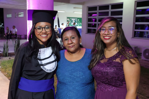 Bruna Rafaela Araújo Lima, concludente de Engenharia Mecânica, foi beneficiária do Auxílio-Moradia. "Por conta dele eu estou aqui hoje. Isso é muito gratificante" (Foto: Viktor Braga/UFC) Imagem: mulher jovem de pele negra vestindo beca abraçada de duas mulheres de pele negra