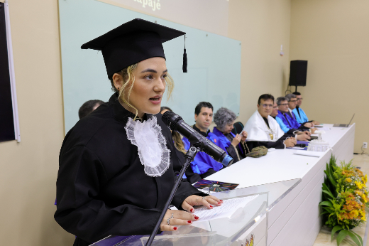 A oradora discente Laura de Lima Mendes agradeceu não apenas àqueles que se tornaram rede de apoio, mas à própria cidade de Itapajé (Foto: Viktor Braga/UFC) Imagem: moça de cabelos loiros e beca preta fala em púlpito