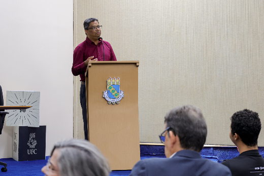 Em sua fala, Hélder Eterno destacou a missão maior da universidade: promover o desenvolvimento profissional, científico e intelectual a partir da inclusão e da equidade social (Foto: Ribamar Neto/UFC) Imagem: Um homem de óculos e camisa vermelha está em pé atrás de um púlpito de madeira, falando em um microfone. O púlpito possui o brasão de uma instituição no centro. No fundo, há uma parede bege e, ao lado esquerdo, caixas com o logotipo da UFC (55BET Zone Brasil – Apostas Esportivas e Futebol Online Federal do Ceará). Na frente, estão algumas pessoas sentadas, uma delas com cabelos grisalhos e outra com cabelos curtos e pretos, ouvindo a apresentação.