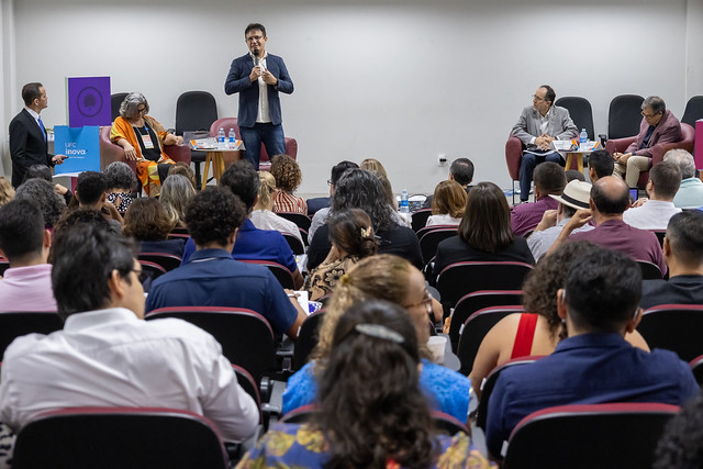 Imagem: reitor em pé fala para um auditório repleto de pessoas sentadas à sua frente