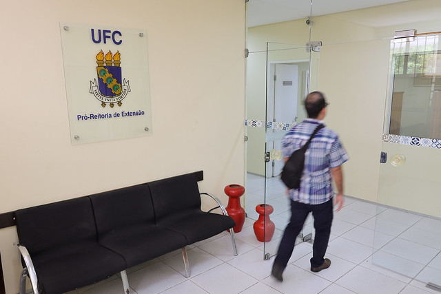 Imagem: entrada de prédio, com sofa preto e homem passando pela porta de vidro.