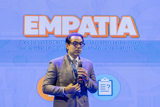 Segundo o diretor do foro da Justiça Federal no Ceará, juiz Julio Coelho, não se pode perder de vista as necessidades e a realidade das pessoas quando se trata de pensar o design de serviços no sistema de Justiça. (Foto: Guilherme Silva/ UFC Informa) Juiz Julio Coelho fala ao microfone na abertura do evento. Ele traja terno cinza. Atrás dele, está um telão azul onde se lê a palavra "empatia".