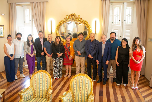 Gestores da UFC e UDA reunidos momentos antes do início da reunião, no Salão Dourado da Reitoria. Encontro oportunizou troca de informações e contatos (Foto: Viktor Braga/UFC) Imagem: Grupo de cerca de treze pessoas posa para foto institucional em uma sala elegante, com piso de madeira, poltronas claras e um grande espelho dourado ao fundo.